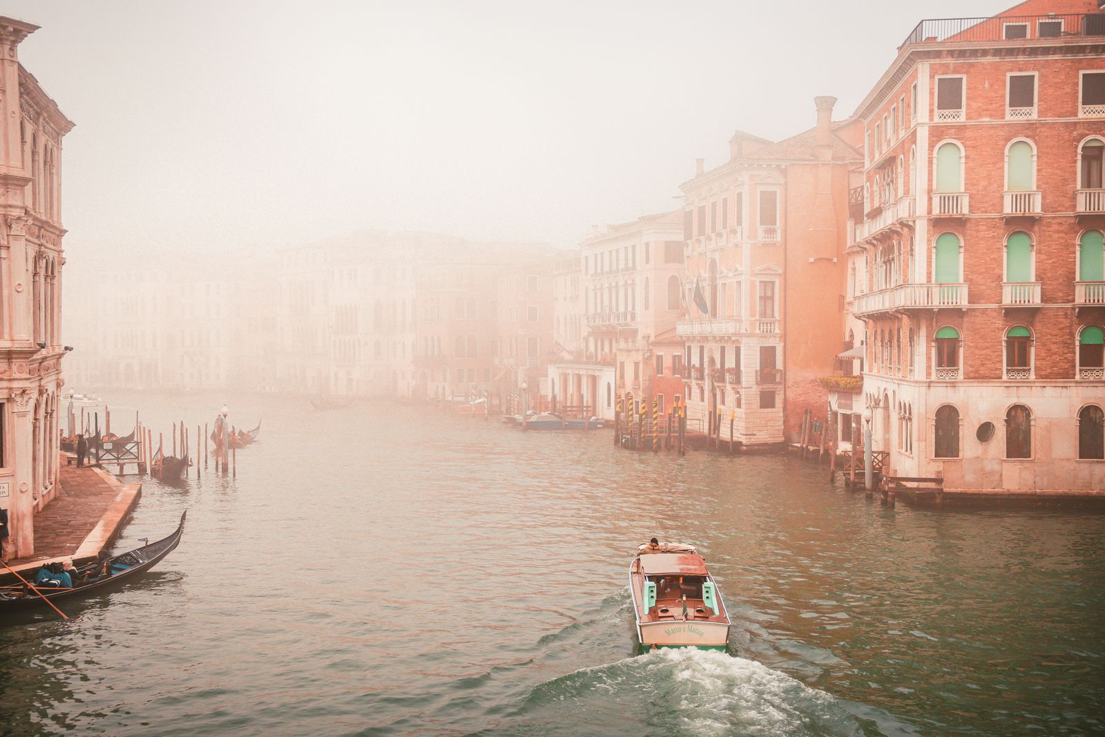 A water taxi and a gondola on Venice's Grand Canal on a misty autumn morning, with palazzi fading into the fog