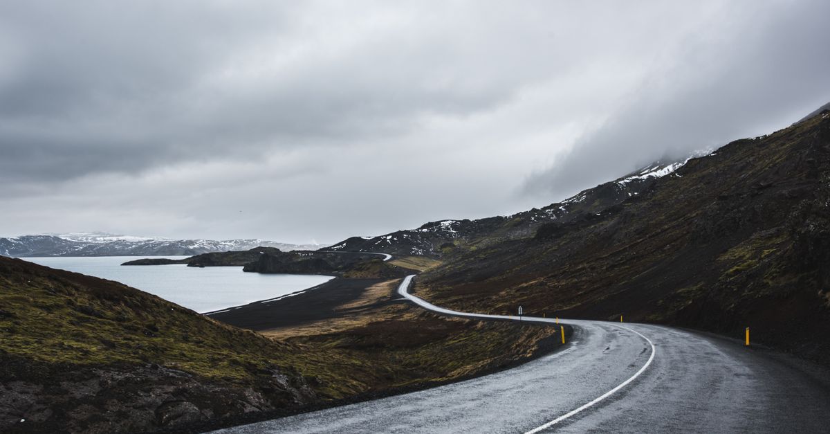 A car on Iceland's Ring Road with snow-capped mountains and a waterfall in the background