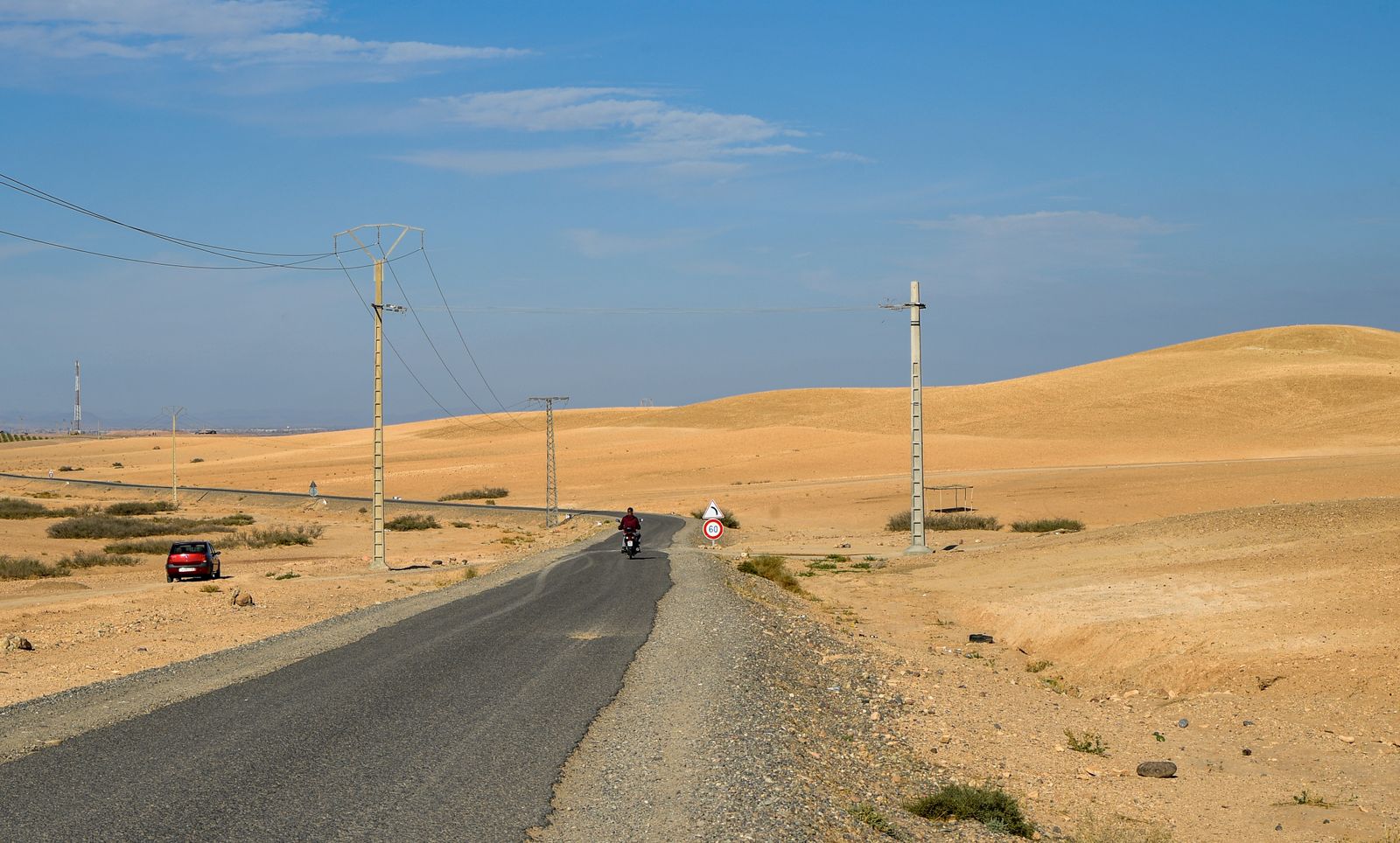 Schmale Asphaltstraße durch die marokkanische Wüste mit Sanddünen und Elektromasten