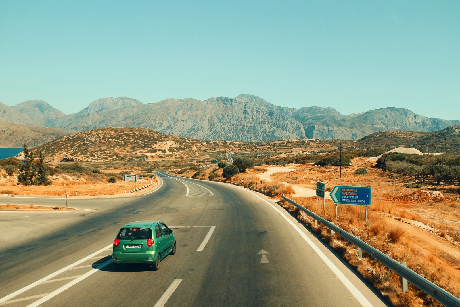 Small car driving down an open road toward distant mountains