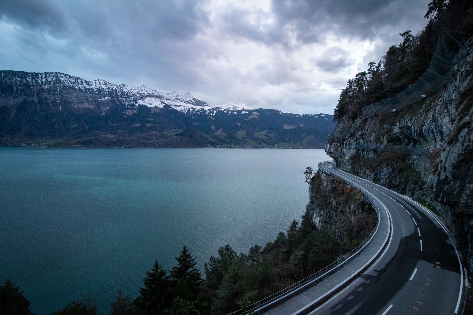 Route sinueuse le long d'un lac suisse avec les Alpes enneigées en arrière-plan