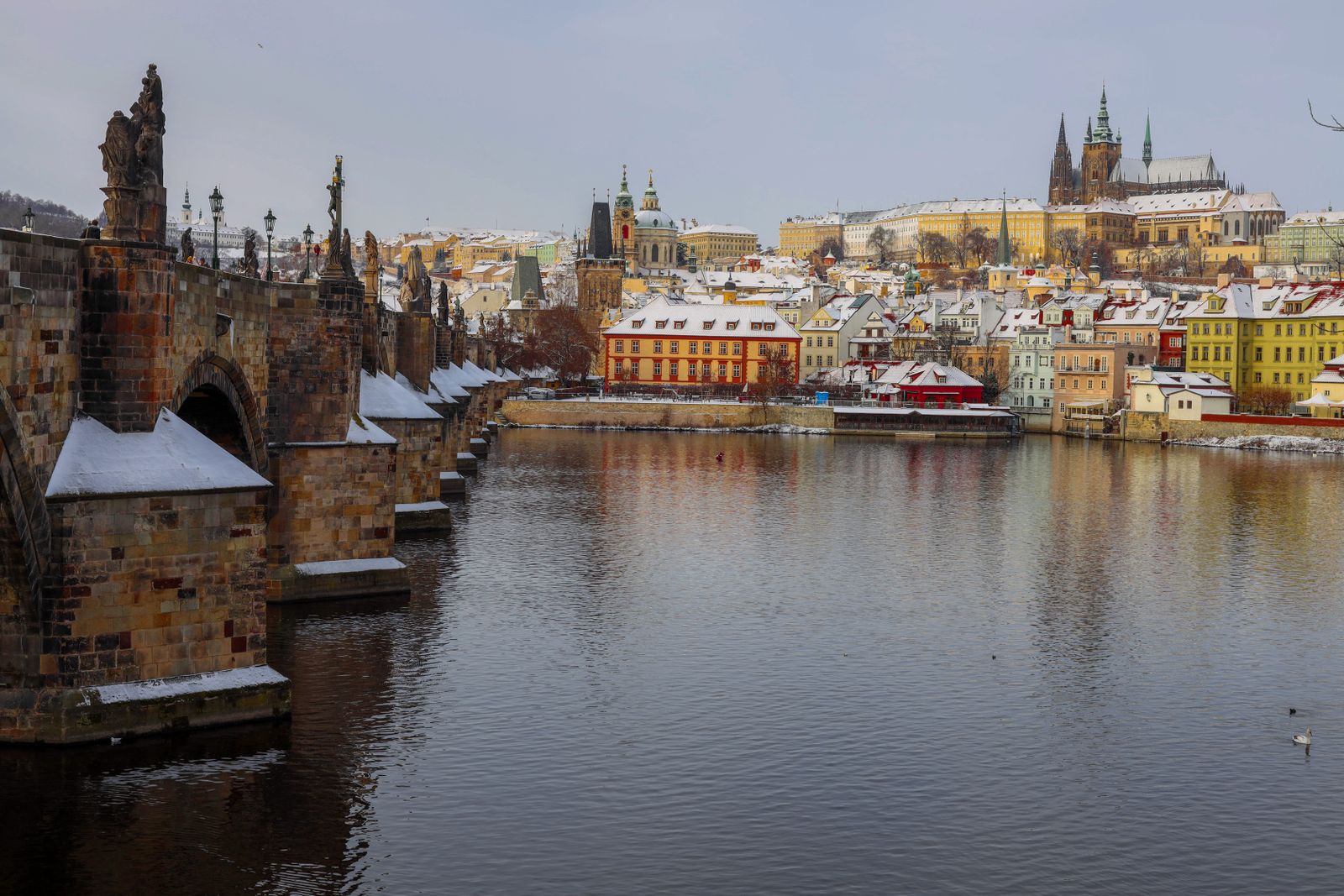 El puente de Carlos y el castillo de Praga cubiertos de nieve junto al río Vltava en un día de invierno