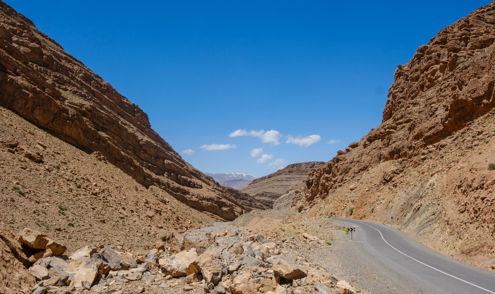 Route goudronnée serpentant au fond d'une gorge rocheuse du Haut Atlas marocain sous un ciel bleu