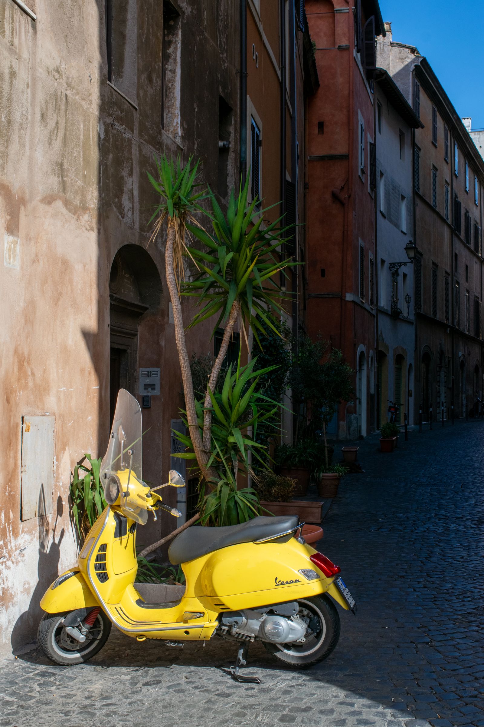 Scooter Vespa jaune gare dans une ruelle pavee de Rome