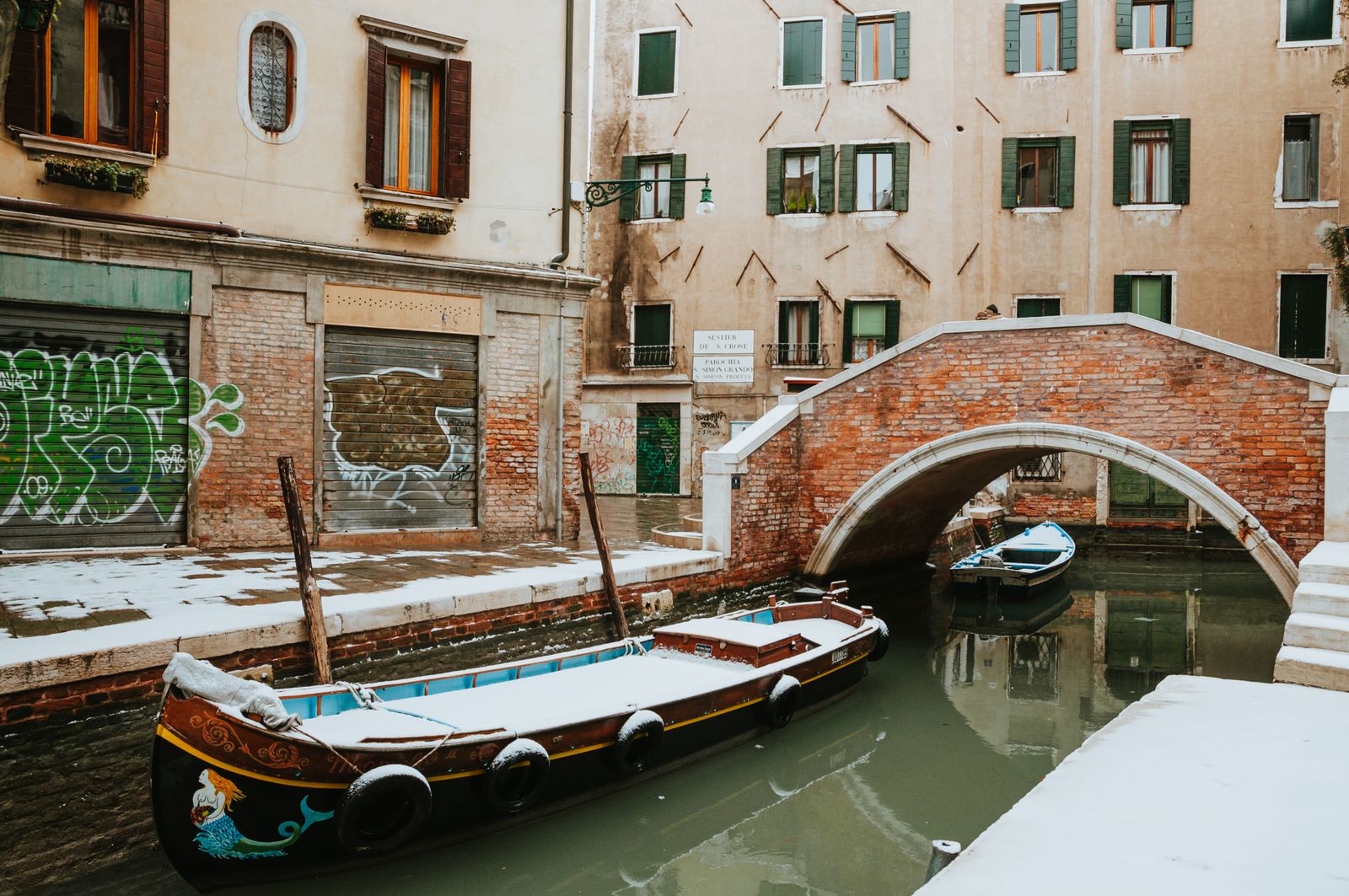 Barcas cubiertas de nieve amarradas en un canal del sestiere de Santa Croce, en Venecia, junto a un puente de ladrillo