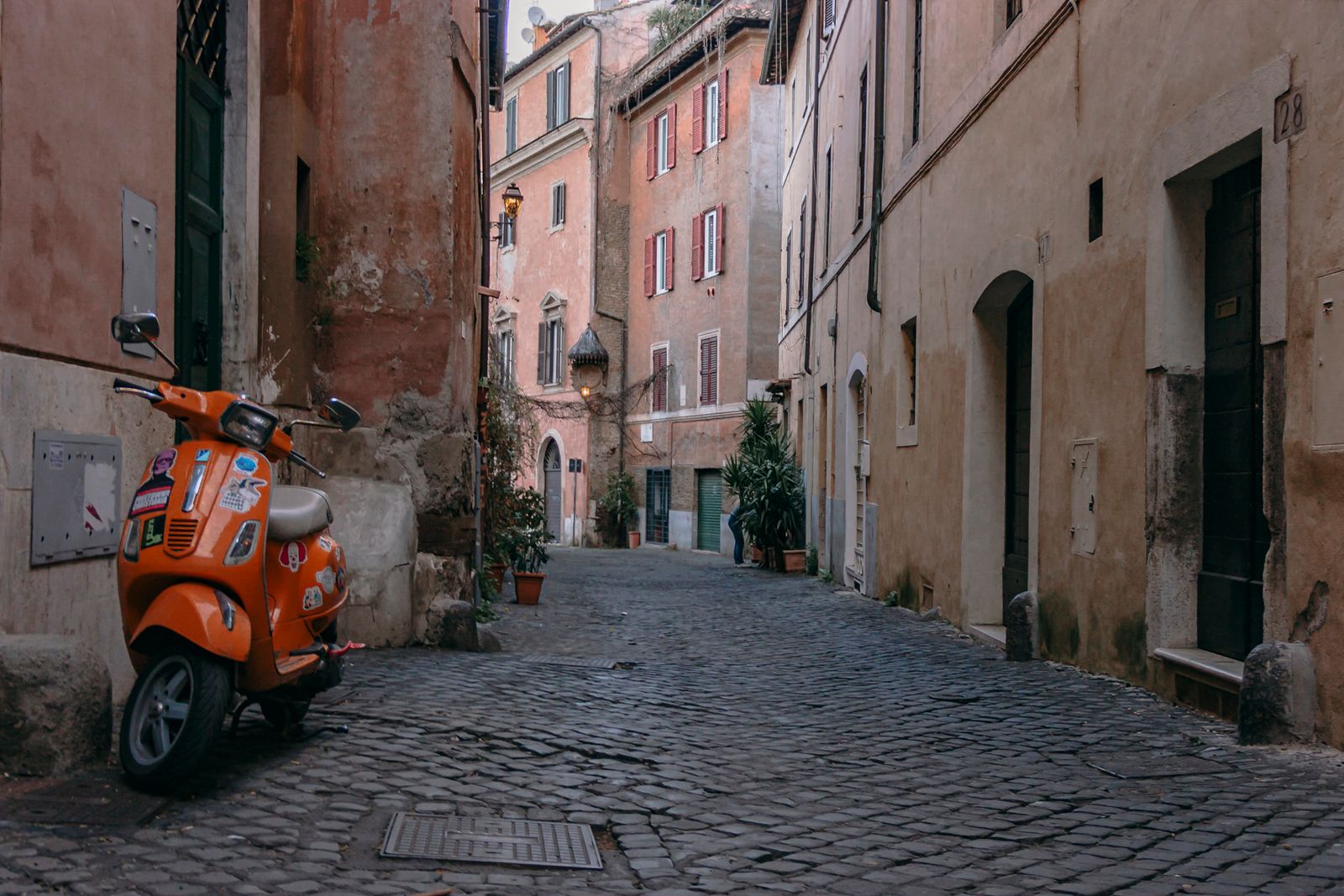 Ruelle pavée déserte du Trastevere à Rome avec un scooter orange garé le long d'un mur ocre