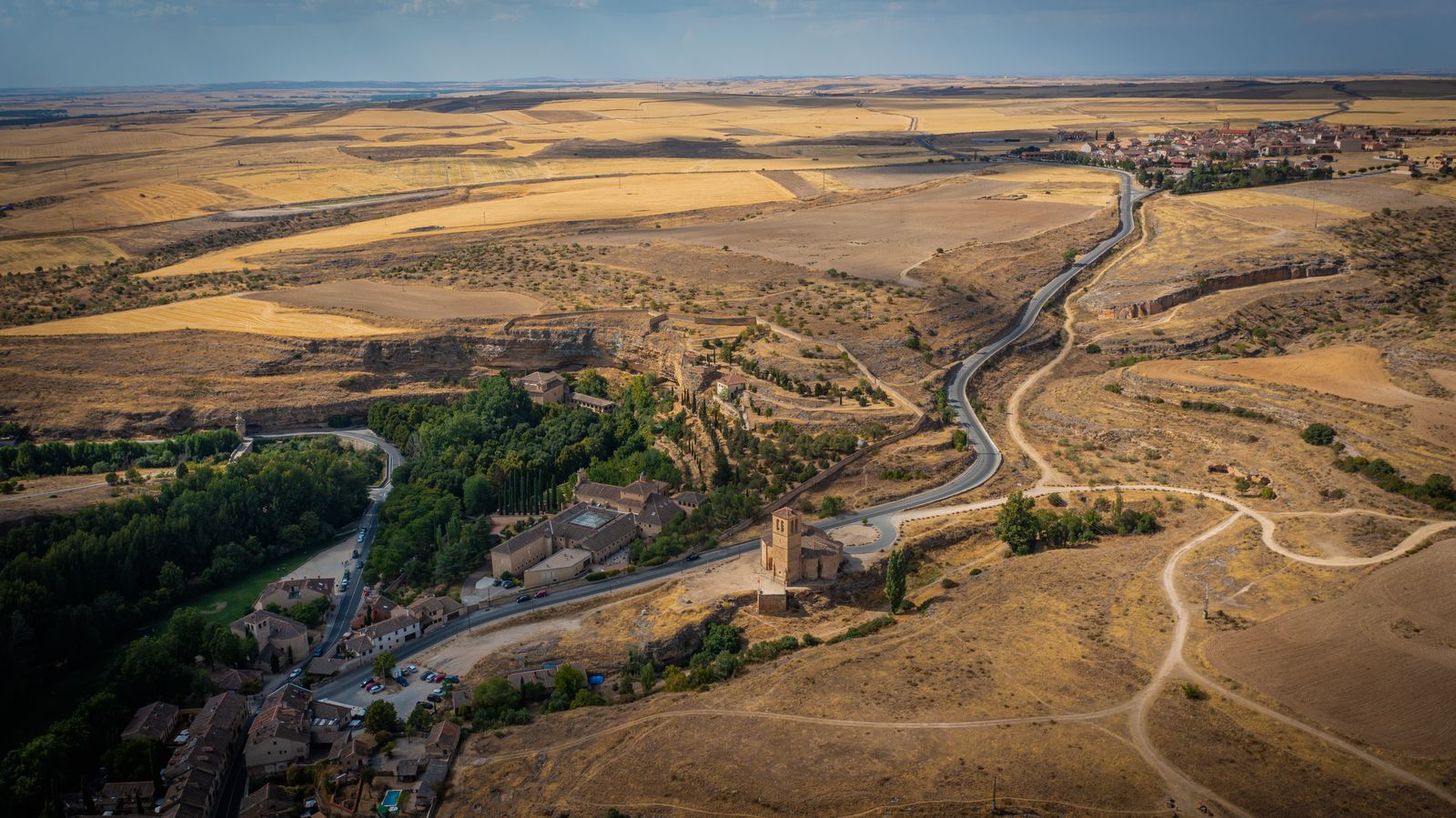 Aerial view of a road winding past a hilltop church through the golden countryside near Segovia, a classic weekend trip from Madrid
